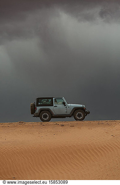 jeep drives across sand dune dirt road on road trip under storm clouds