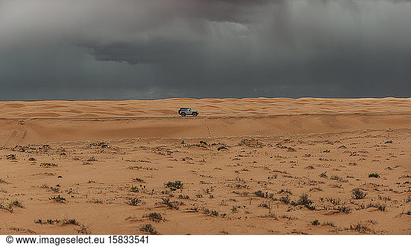 Jeep drives through the sand dunes of Utah under stormy skies