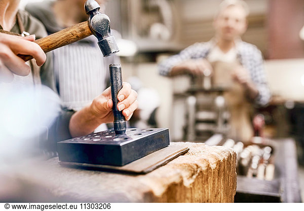 Jeweler using hammer and equipment in workshop