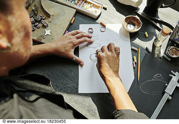 Jeweller sketching ring design on paper at workbench