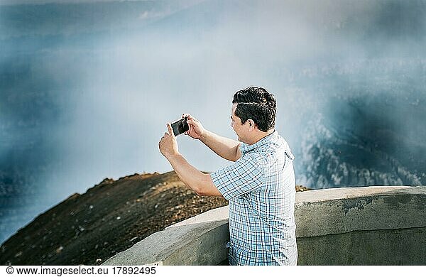 Joven turista tomando fotos en un mirador volcánico. Hombre aventurero con su celular tomando fotos en un mirador  Turista tomando fotos en un mirador