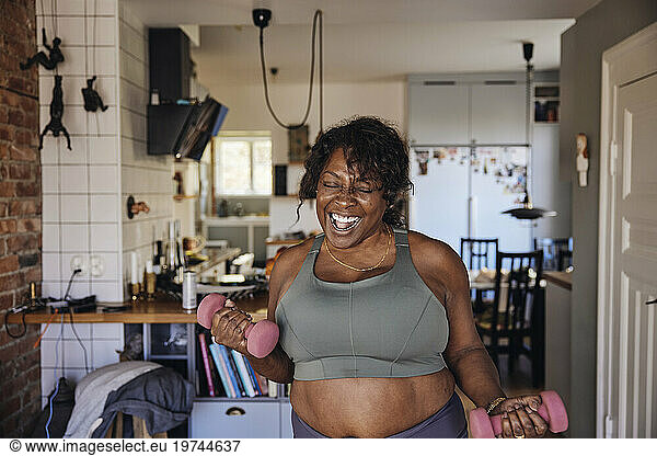 Joyful mature woman dancing and exercising with dumbbells at home