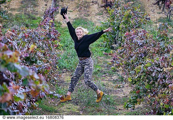 Joyful mature young blondy farmer woman jumping in a vineyard farmland. Iguzkiza  Navarre  Spain  Europe.