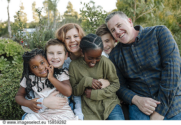 Joyful mixed-race family with four children hugging outdoors