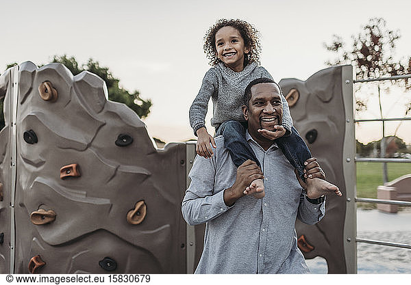 Joyful son sitting on a happy father's shoulders at park playground