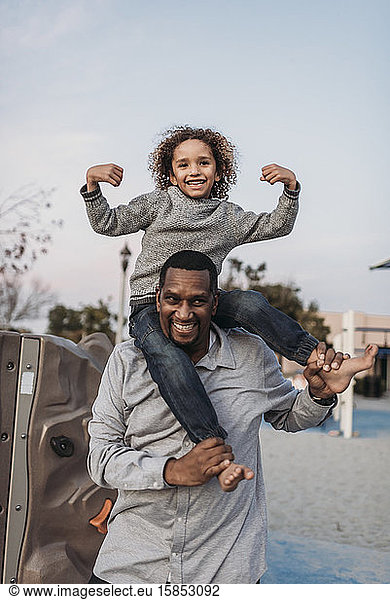 Joyful son sitting on happy father's shoulders at park playground