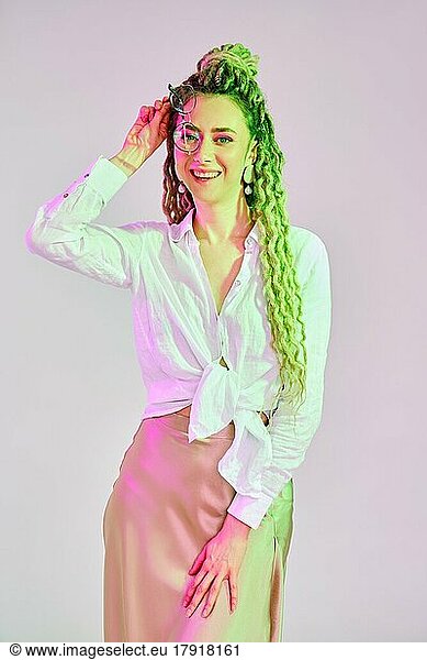 Joyful woman plays with spectacles under colorful lights in the studio