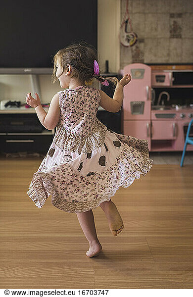 Joyous 4 yr old in tiered dress dancing barefoot on hardwood floor