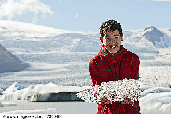 Jugendlicher hält Eis von einer Gletscherlagune in Island hoch