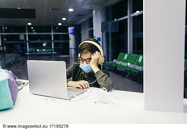 Jugendlicher mit Maske besucht Online-Kurse im Flughafenterminal
