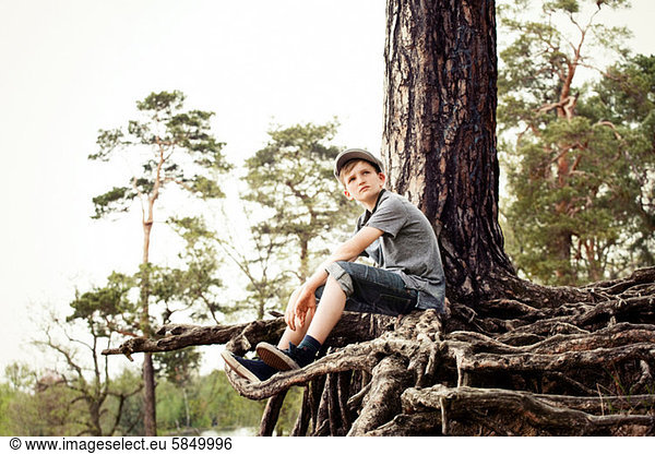 Junge auf Wurzeln eines Baumstammes sitzend