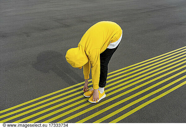 Junge berührt Zehen  während er sich über gelbe Markierungen auf der Straße beugt