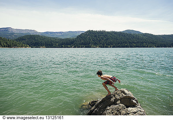 Junge beugt sich auf Felsen am See gegen den Himmel