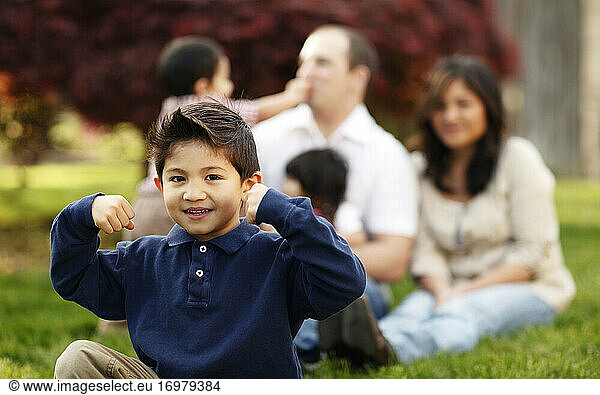 Junge  der vor seiner Familie im Gras sitzt und sich beugt