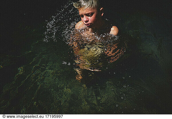 Junge durchbricht Wasseroberfläche mit großem Stein