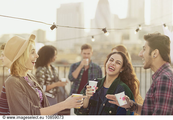 Junge erwachsene Freunde beim Lachen und Trinken auf der Dachparty