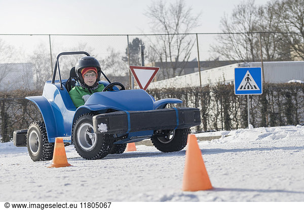 Junge fährt elektrisches Spielzeugauto auf schneebedeckter Straße
