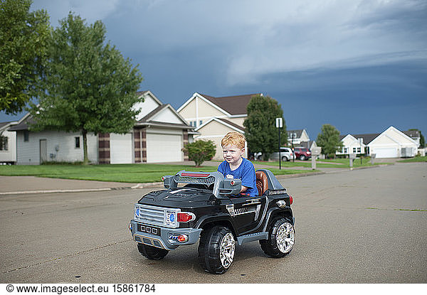 Junge fährt elektrisches Spielzeugauto in der Nachbarschaft