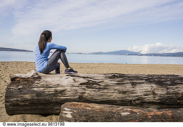 Junge Frau auf einem Baumstamm sitzend Blick auf die englische Bucht Vancouver Kanada