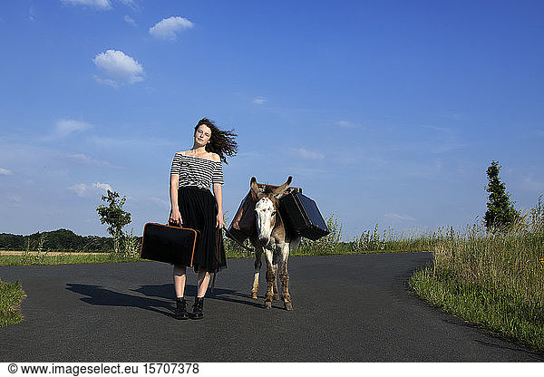 Junge Frau auf Landstraße mit Esel  der Gepäck trägt