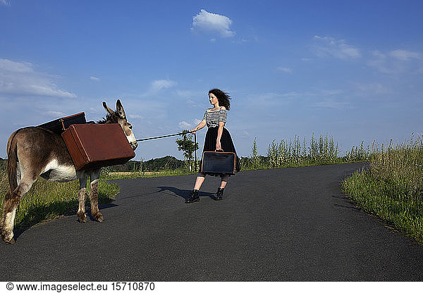 Junge Frau auf Landstraße mit Esel  der Gepäck trägt