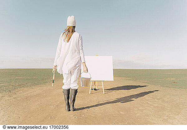 Junge Frau auf trockenem Feld  beginnt auf weißer Leinwand zu malen