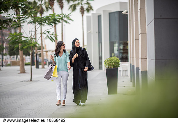 Junge Frau aus dem Nahen Osten in traditioneller Kleidung geht mit einer Freundin die Straße entlang  Dubai  Vereinigte Arabische Emirate