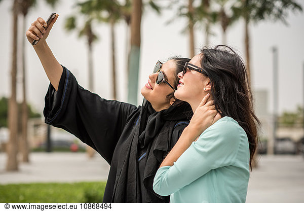 Junge Frau aus dem Nahen Osten in traditioneller Kleidung mit Smartphone-Selfie mit Freundin  Dubai  Vereinigte Arabische Emirate