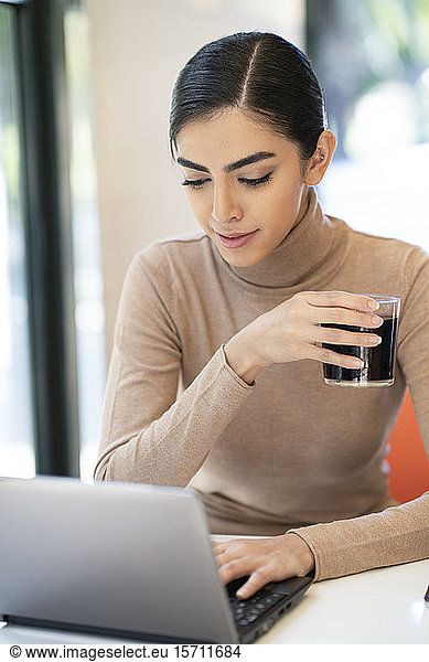 Junge Frau bei einem Drink und mit Laptop in einem Café