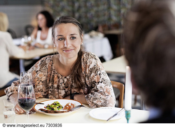 Junge Frau beim Anblick eines Freundes am Restauranttisch mit Menschen im Hintergrund