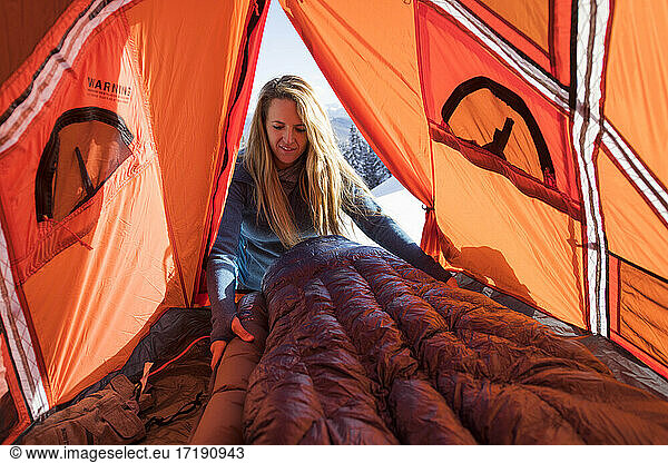 Junge Frau beim Aufbauen des Schlafsacks im Zelt beim Wintercamping