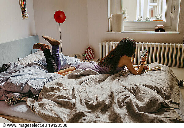 Junge Frau benutzt ein Mobiltelefon  während sie zu Hause auf dem Bett liegt