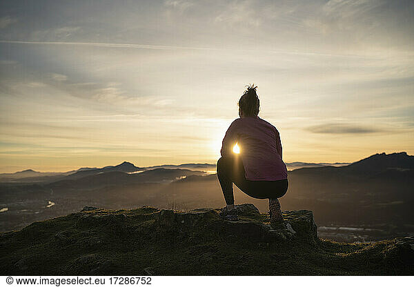 Junge Frau betrachtet den Sonnenaufgang  während sie auf einer Klippe kauert