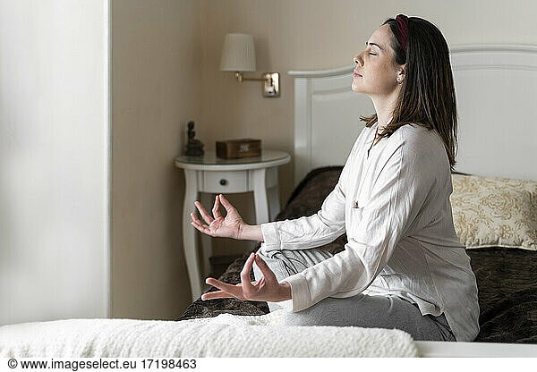 Junge Frau übt Padmasana im Sitzen auf dem Bett
