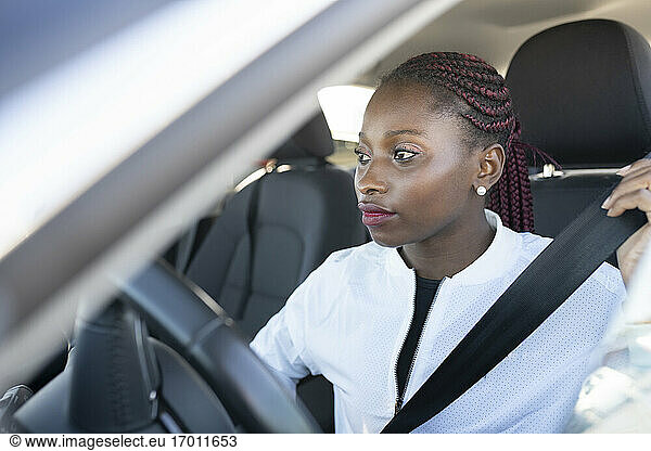 Junge Frau  die den Sicherheitsgurt anlegt  während sie im Auto sitzt