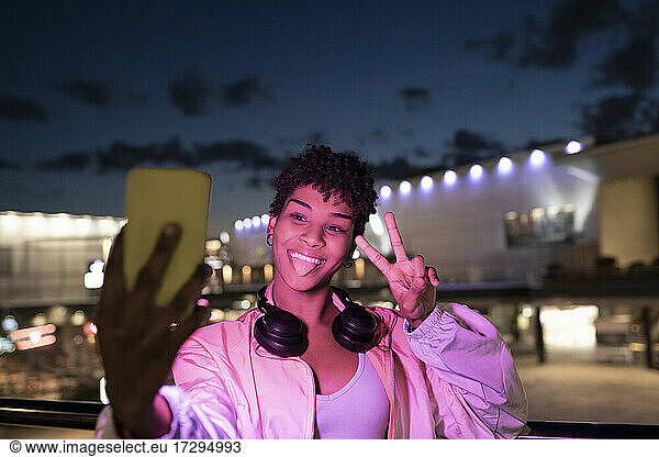 Junge Frau  die ein Selfie mit ihrem Smartphone macht  während sie in der Nacht positive Emotionen zeigt