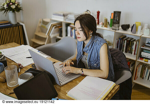 Junge Frau  die einen Laptop benutzt  während sie eine Schulaufgabe zu Hause erledigt