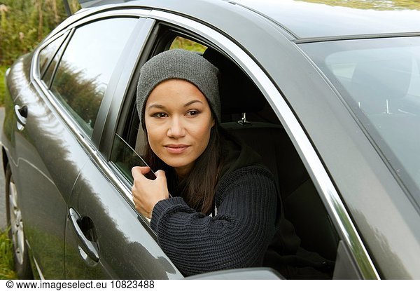 Junge Frau  die sich lehnt und aus dem geparkten Autofenster blickt