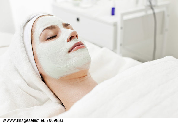 Junge Frau entspannt auf Massagetisch mit Gesichtsmaske im Beauty Spa