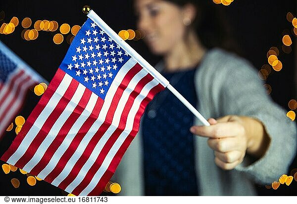 Junge Frau hält eine amerikanische Flagge mit funkelnden Licht Bokeh Hintergrund  Usa Konzept bunt.