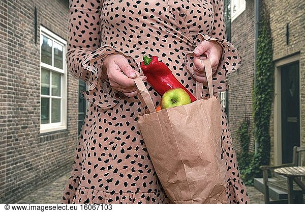 Junge Frau hält eine Tüte mit frischem Gemüse und Obst auf der Straße in der Stadt  Äpfel und Paprika in Großaufnahme.