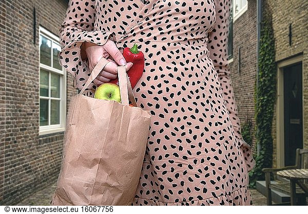 Junge Frau hält eine Tüte mit frischem Gemüse und Obst auf der Straße in der Stadt  Äpfel und Paprika in Großaufnahme.
