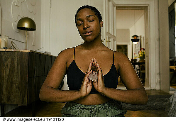 Junge Frau hält Stein beim Meditieren zu Hause