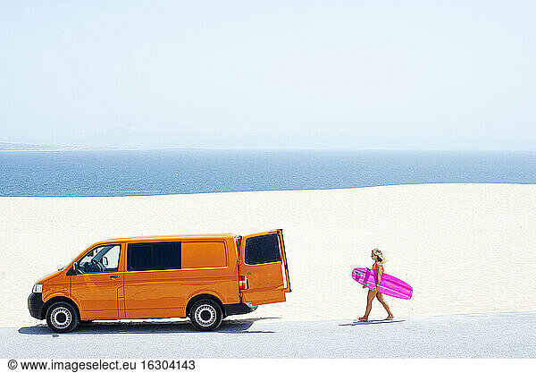 Junge Frau hält Surfbrett beim Spaziergang am Strand an einem sonnigen Tag