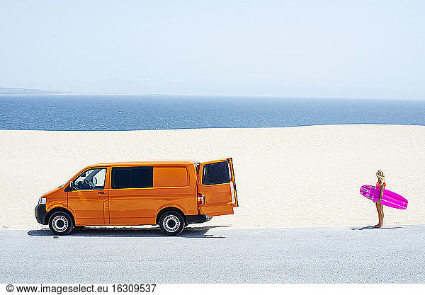 Junge Frau hält Surfbrett und steht am Strand an einem sonnigen Tag