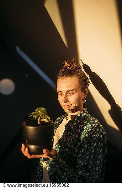 Junge Frau hält zu Hause Pflanze im Blumentopf