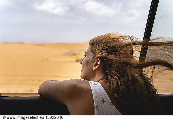 Junge Frau im Auto  die sich in der Wüste Sahara aus dem Fenster lehnt  Merzouga  Marokko