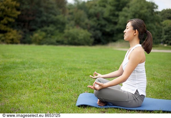 Junge Frau im Park praktiziert Yoga-Lotus-Position