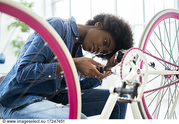 Junge Frau in Freizeitkleidung repariert Fahrrad zu Hause