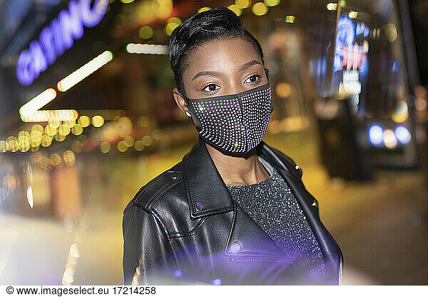 Junge Frau in funkelnden Maske in der Stadt mit Lichtern in der Nacht